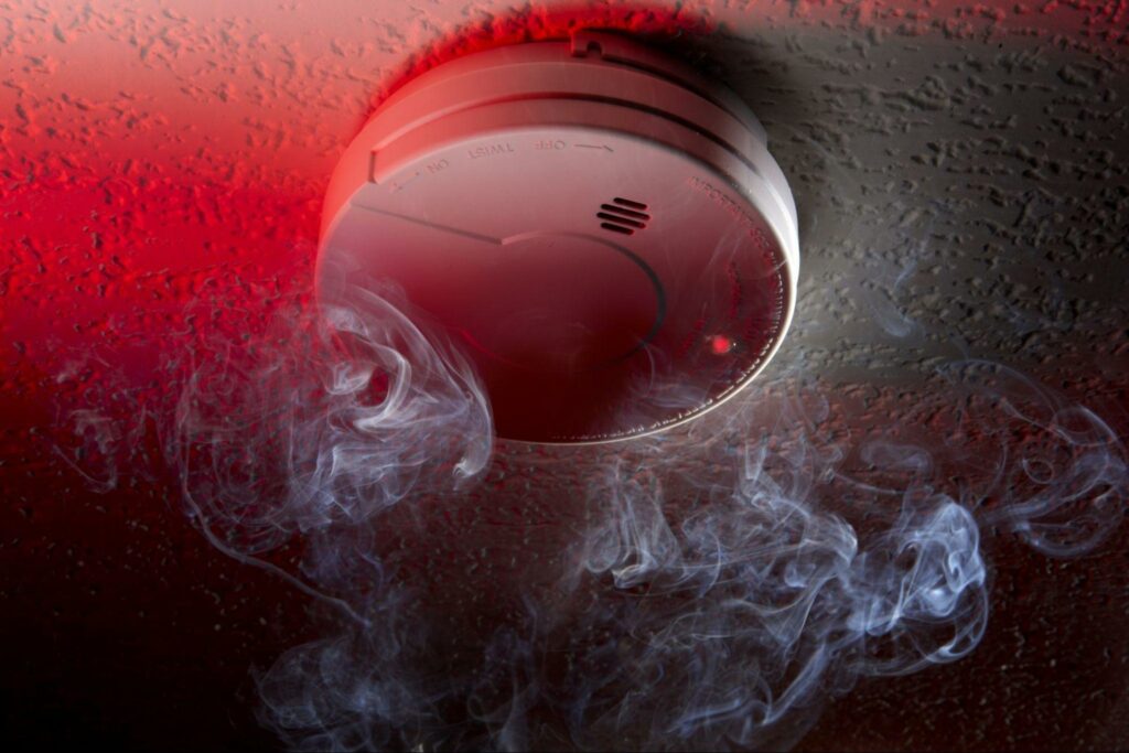 A fire alarm on a ceiling with smoke swirling up towards it